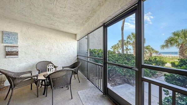 A balcony with wicker furniture, a view of the beach, and a sign with beach rules. - Firethorn 111- Gorgeous, fully remodeled 2BR/2BA beachfront (Siesta Key)