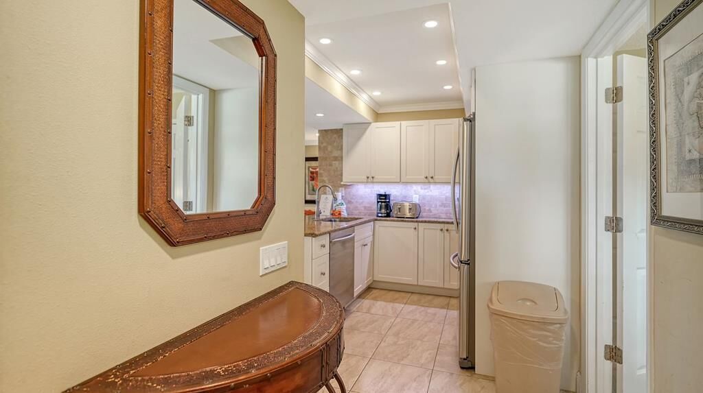 A compact kitchen with white cabinets, a coffee maker, and a trash bin.