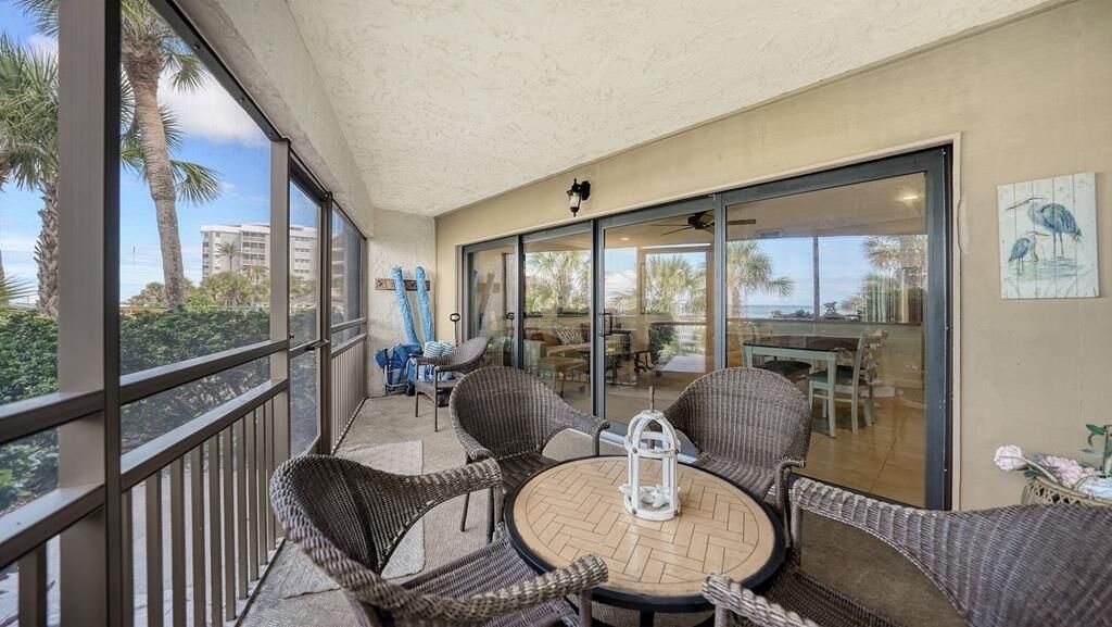 Une terrasse extérieure couverte, aménagée avec des meubles en osier et une table ronde, et de grandes portes-fenêtres coulissantes qui donnent sur un espace intérieur comprenant une table à manger et des chaises.