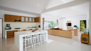 Een moderne keuken met houten kastjes, een eethoek met witte stoelen en een woonruimte met een bank en televisie.