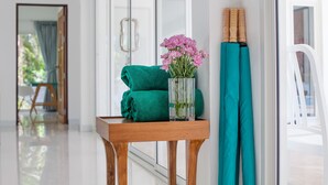 Een houten tafel met een vaas roze bloemen, een groene handdoek en een blauwgroene handdoek tegen een witte muur.