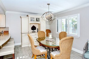 A dining area with a round glass table, wicker chairs, and a chandelier.