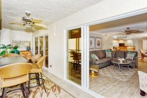 A spacious living area with a sofa, coffee table, and dining table set with wicker chairs.