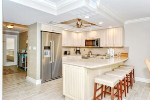 A modern kitchen with a central island, stainless steel appliances, and a ceiling fan.