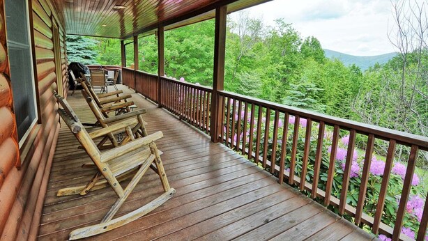 A wooden deck with rocking chairs, a covered area, and a view of dense green forest and mountains.