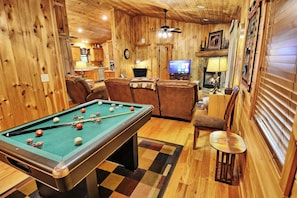 A pool table in a room with wooden walls, a television, and a fireplace.