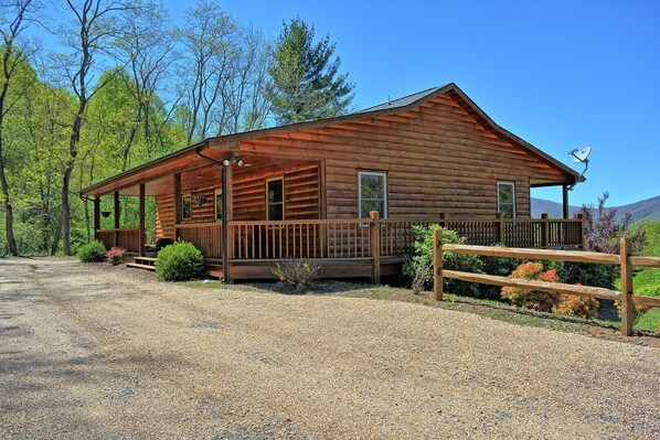 A log cabin with a porch, a fenced area, and a gravel driveway.