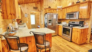 A wooden cabin-style kitchen with a central island, two bar stools, stainless steel appliances, and a microwave.