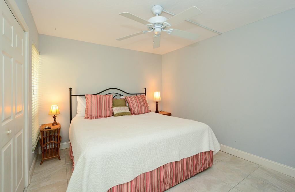 A bedroom with a bed, two bedside lamps, a ceiling fan, and a window with blinds.