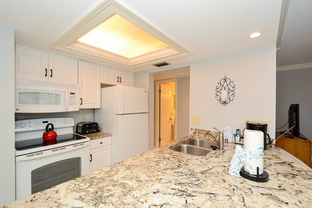 A kitchen with white cabinets, a microwave, a stove, a kettle, a sink, and a coffee maker.