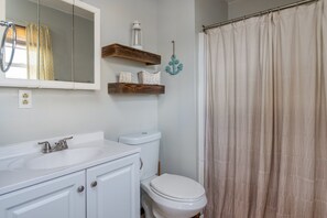 A bathroom with a white sink, a toilet, and a shower curtain. There are wooden shelves above the toilet with a lantern and baskets.