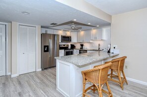 A modern kitchen with white cabinetry, stainless steel appliances, a granite countertop, and a ceiling fan.