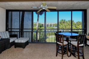 A balcony with a view of a lake and palm trees, a ceiling fan, and a dining table with chairs. - Doveplum 621- Newly remodeled and refurnished 2BR/2.5BA townhome (Siesta Key)
