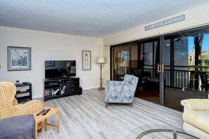 A living room with a television, a sofa, a chair, and a glass door leading to a balcony. - Doveplum 621- Newly remodeled and refurnished 2BR/2.5BA townhome (Siesta Key)