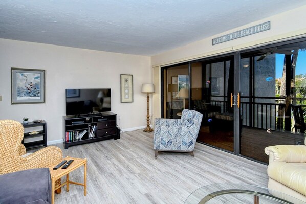A living room with a television, a sofa, a chair, and a glass door leading to a balcony.