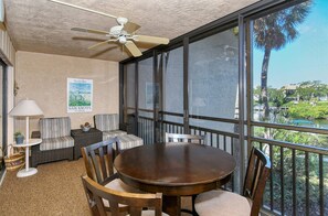 A sunroom with a large window, a ceiling fan, a dining table with chairs, a striped sofa, and a small lamp. - Doveplum 621- 2 Story, 2 Bedroom Condo with Private Beach with lounge chairs & umbrella provided,... (Siesta Key)