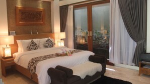 Um quarto espaçoso com uma cama grande, cabeceira de madeira, mesa de cabeceira com abajur e vista para um jardim através de uma porta de vidro.