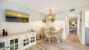 A dining area with wicker chairs, a white cabinet with glass doors, and a hanging light fixture.