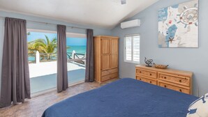 A bedroom with a bed, a wooden dresser, a ceiling fan, a map on the wall, and a view of the ocean through the window. - Private Oasis On The Beach (Progreso)