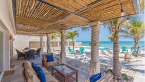 A covered outdoor seating area with wicker furniture, a glass table, and a view of the beach and ocean. - Private Oasis On The Beach (Progreso)