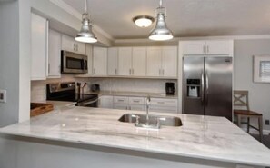 A modern kitchen with white cabinets, stainless steel appliances, and a marble island.