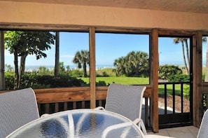 A covered outdoor seating area with a view of the ocean and greenery.