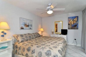 A bedroom with a bed, two bedside lamps, a ceiling fan, a television, and artwork on the walls.