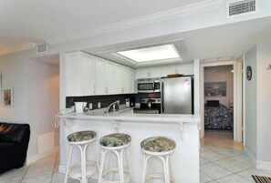 A modern kitchen with white cabinets, a central island with stools, a microwave, and a refrigerator.