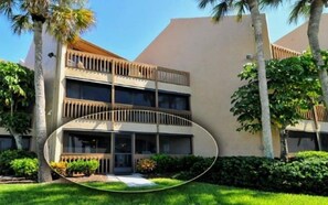 A multi-story hotel with balconies, surrounded by greenery and palm trees.