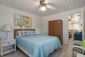 A bedroom with a bed, a nightstand, a wooden wardrobe, a map artwork on the wall, and a view into the living area.
