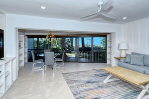 A modern living room with a sofa, a coffee table, a TV, and a dining area with chairs and a table. - Doveplum 112- 4 bedroom/3.5 bath beachfront townhouse ! (Siesta Key)