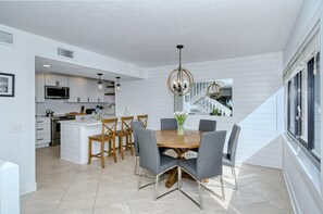 A modern kitchen with white cabinetry, a central island, and a dining area with a wooden table and grey chairs.
