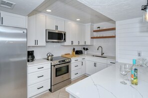 A modern kitchen with white cabinetry, a stainless steel refrigerator, a microwave, a stove, and a sink. - Doveplum 112- 4 bedroom/3.5 bath beachfront townhouse ! (Siesta Key)