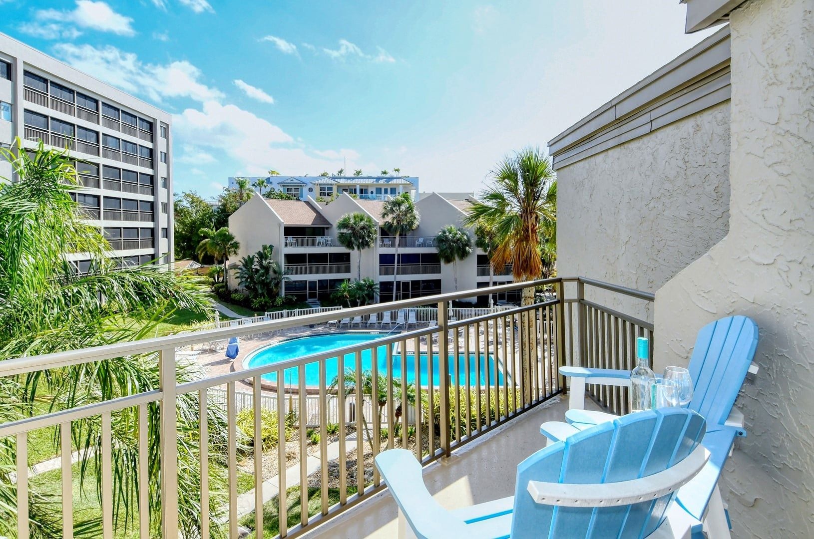 A balcony with a pool, lounge chairs, and a view of a hotel building.