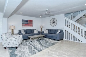 A modern living room with a sectional sofa, a coffee table, a patterned armchair, a rug, a wall clock, and an American flag. - Doveplum 112- 4 bedroom/3.5 bath beachfront townhouse ! (Siesta Key)