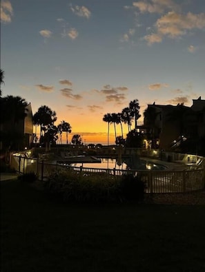 A resort with a pool area, palm trees, and buildings in the background during sunset.