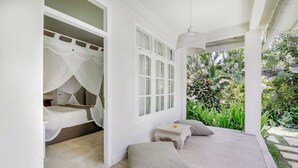 Un dormitorio con cama bajo dosel, una mesita de noche con lámpara, y vista a un jardín exuberante.