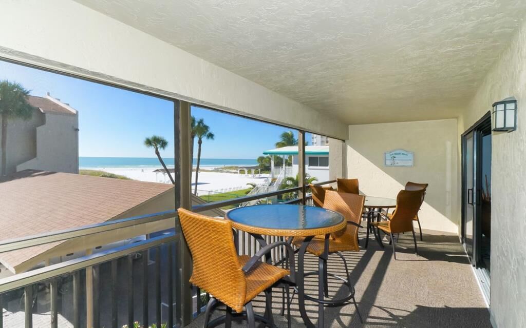 Ein Balkon mit Blick auf den Strand, Korbmöbel, ein runder Tisch und ein kleines Schild an der Wand.