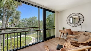 Un balcon donnant sur un plan d’eau et sur un espace verdoyant, aménagé avec des fauteuils en osier et un bureau.