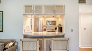 A compact kitchen with a microwave, toaster, and coffee maker. There are two wicker chairs and a small table in front.