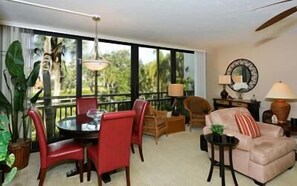 Une pièce comprenant une table à manger, des chaises, un canapé, une lampe et de grandes fenêtres offrant une vue dégagée.
