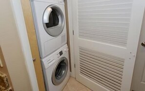 Une buanderie avec des machines à laver superposées et une porte fermée dotée d’une grille d’aération.