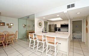 A modern kitchen with white cabinetry, a central island with bar stools, and a dining area with a glass partition.
