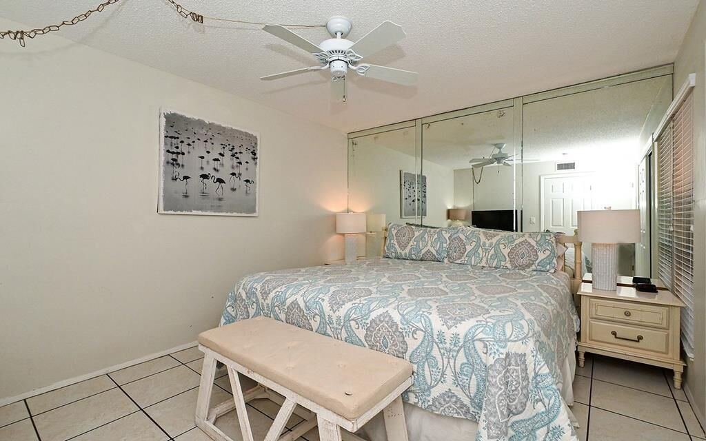 A bedroom with a bed, a bench, a ceiling fan, a large mirror, and a wall art piece.