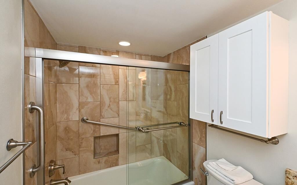 A bathroom with a glass-enclosed shower, a white toilet, and a white cabinet above the toilet.