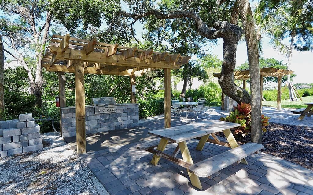 Een houten pergola met picknicktafels en stenen banken in een aangelegde tuin.