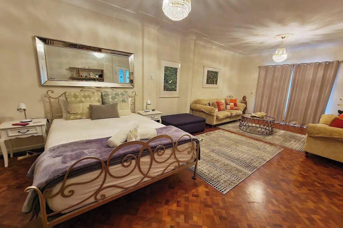 A bedroom with a bed, a sofa, a small table, and a chandelier.