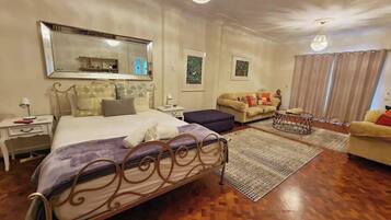 A bedroom with a bed, a sofa, a small table, and a chandelier.