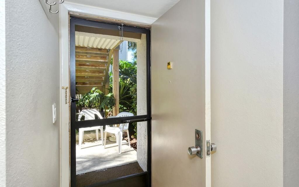 Puerta que da a un patio exterior con una silla y una mesa blancos.