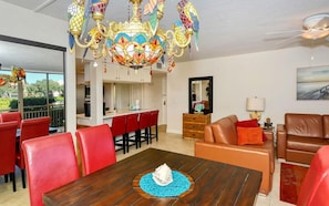 A dining area with a wooden table, red chairs, and a colorful chandelier. - Firethorn 610- 2 bedroom 1.5 bath condo with private beach access (Sarasota)